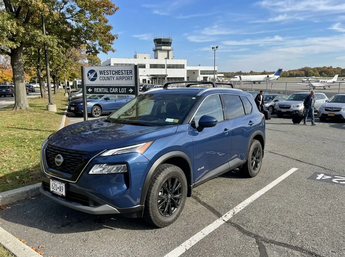 Dark blue Nissan Rogue compact SUV at HPN airport car rental lot, Westchester NY, crisp exterior photo showing all terrain capability